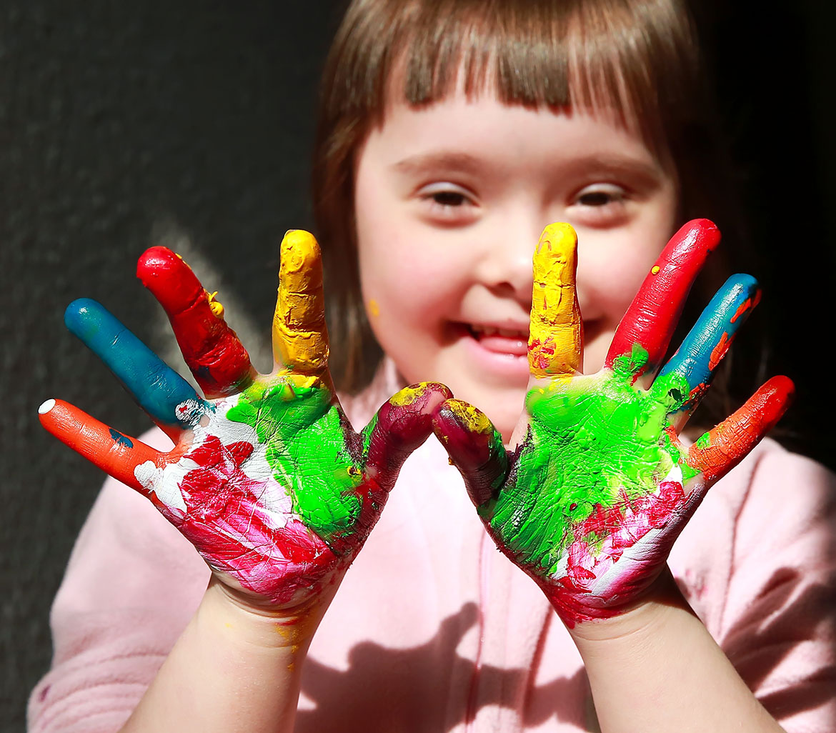 young girl smiling with both hands in multicolour paint