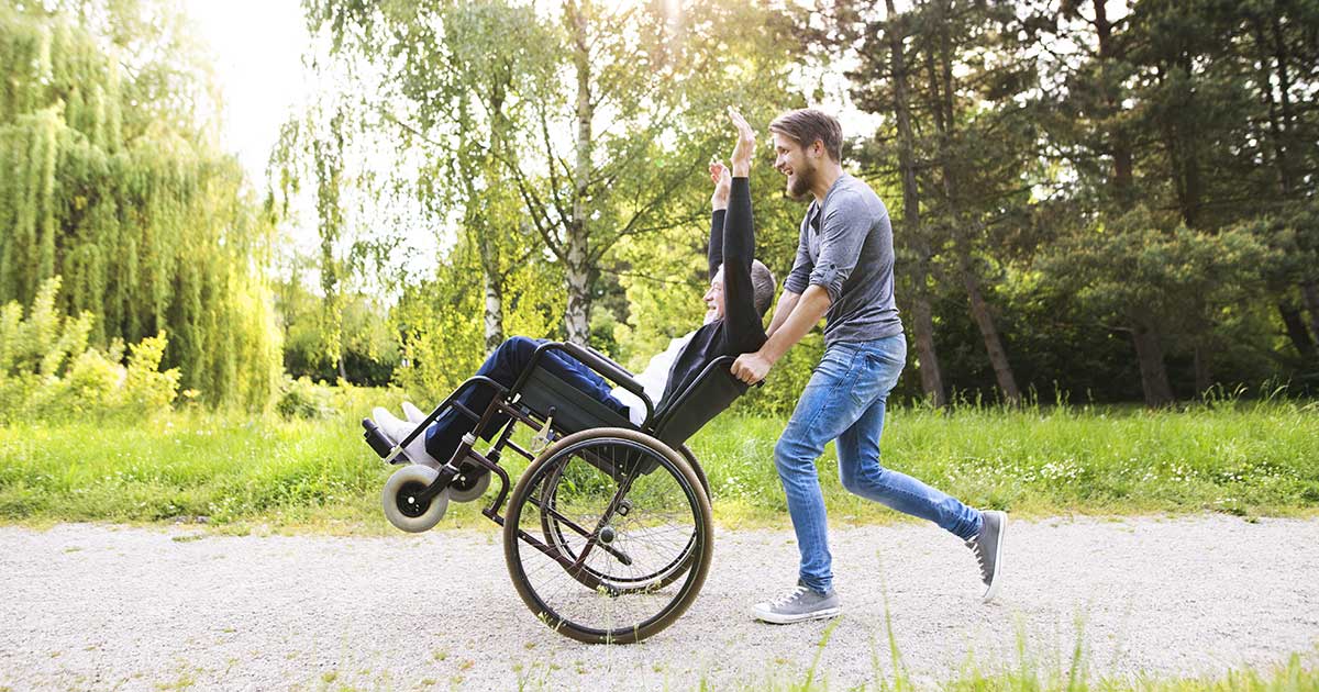 Male Support Worker running with man in wheelchair at the park
